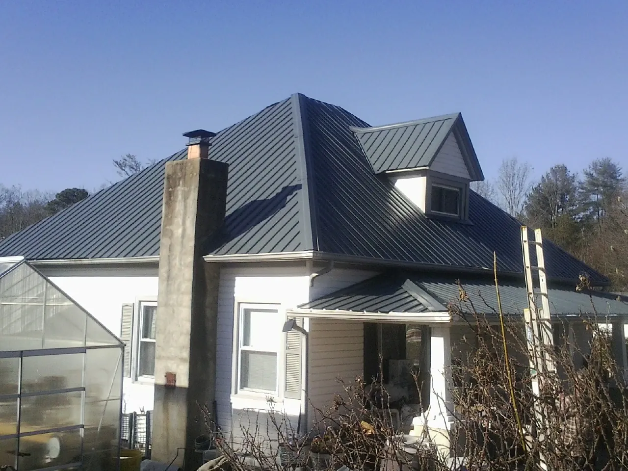 Dark blue standing seam metal roof on a white farmhouse with dormer — Slate & Tile Roof Repair by Roofing Brothers in Evangeline