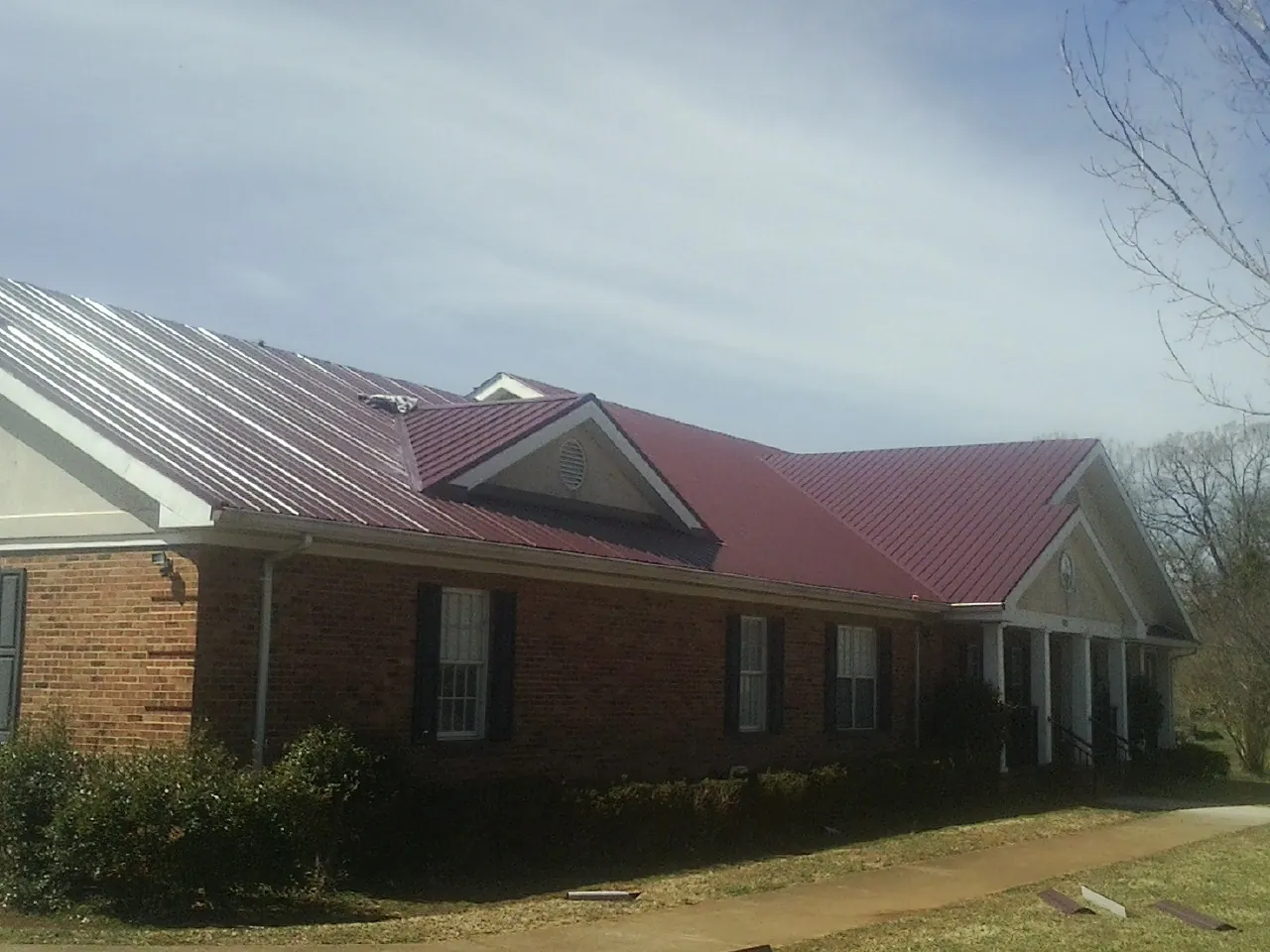 Red metal roof with gabled entries on a long brick building, from a Hail Damage Roof Repair job in Evangeline