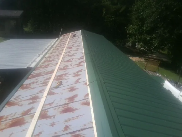 Old rusted panels beside newly installed green metal roofing — Wind Damage Roof Repair by Roofing Brothers in Evangeline