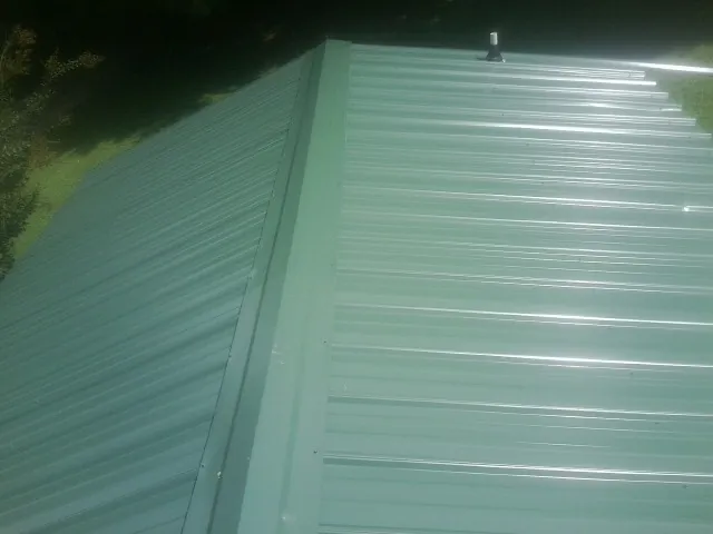New green metal panels meeting at the ridge of a roof — Flat Roof Repair work by our crew in Evangeline