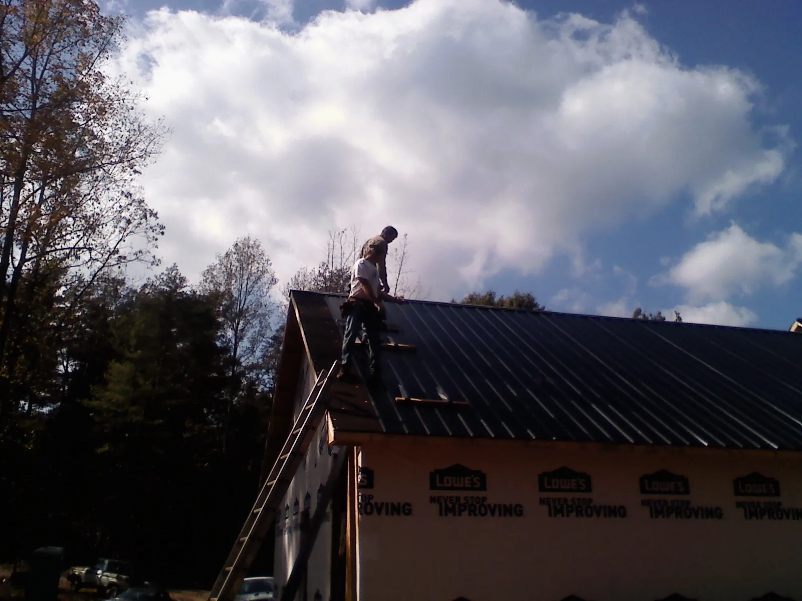 Roofer fastening dark metal panels high against a cloudy sky, from a Roof Inspection job in Evangeline