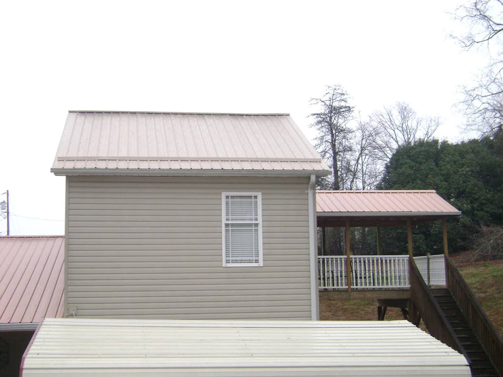 Tan metal roofs on a two story addition and attached porch, from a Roof Replacement job in Evangeline